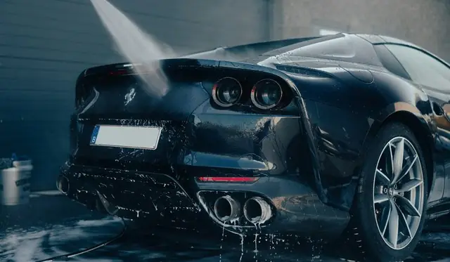 Dark sports car being rinsed with a pressure washer